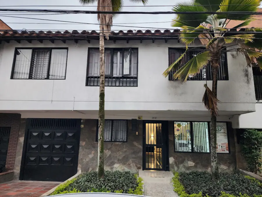 Fachada de Candamil: casa blanca de dos pisos con palmas